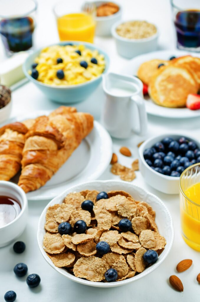 Breakfast table setting with flakes, juice, croissants, pancakes